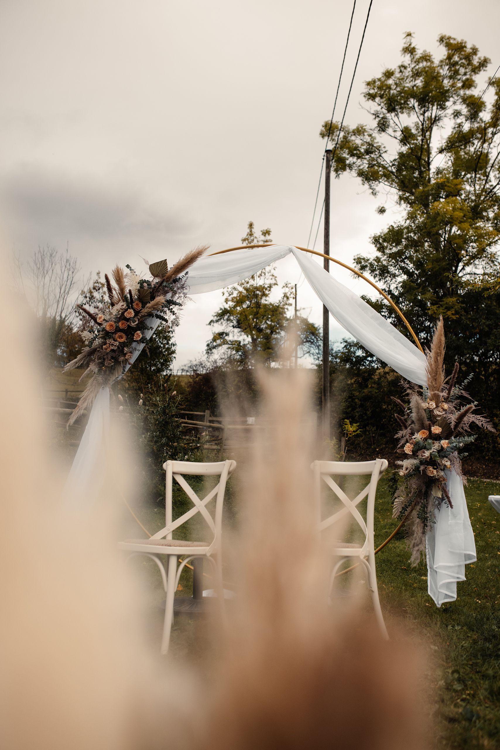 Runder Trau-Bogen aus Gold mit Chiffon und Trockenblumen im Traugarten des Quellhofs