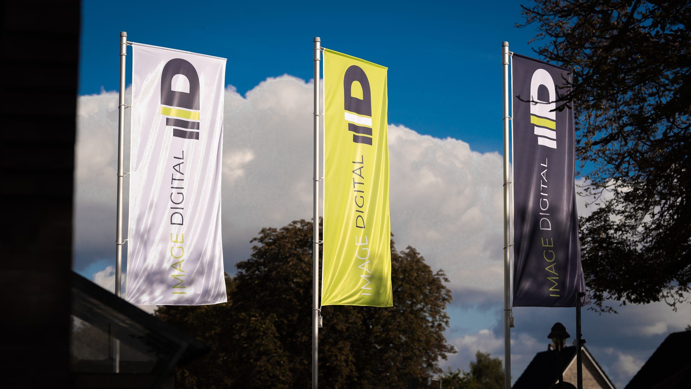 Drei Image-Digital-Fahnen in Grün, Weiß und Anthrazit vor blauem Himmel.