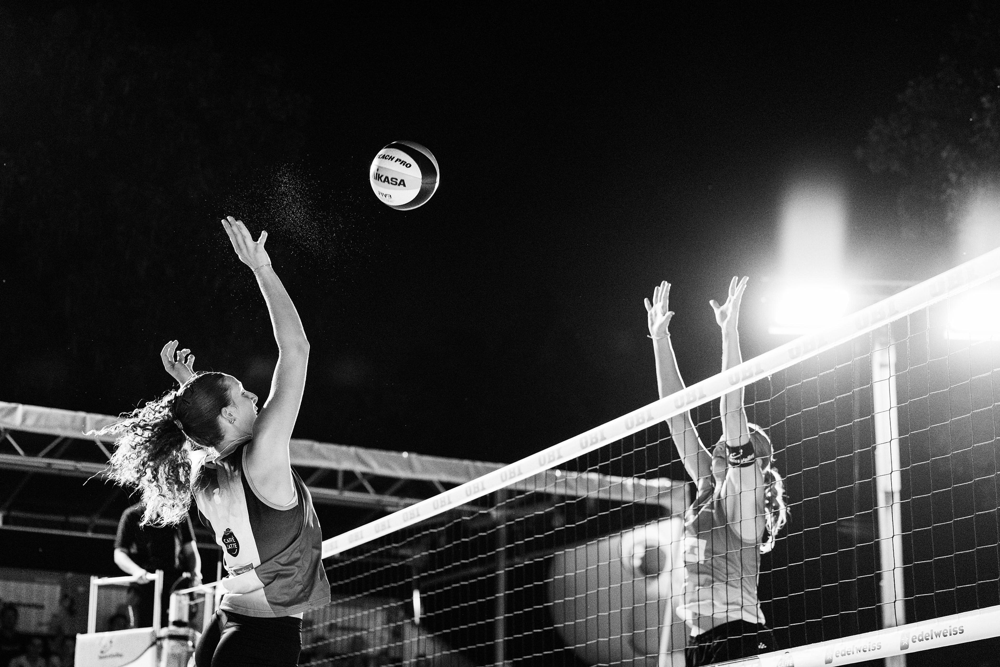 Elin Shana Kluser im Angriff gegen den Block von Annique Niederhauser, Schwarzweißaufnahme unter Flutlicht, im Spiel Bentele/Niederhauser gegen Kluser/Grünig bei der OBI Beach Tour 2026 in Luzern.