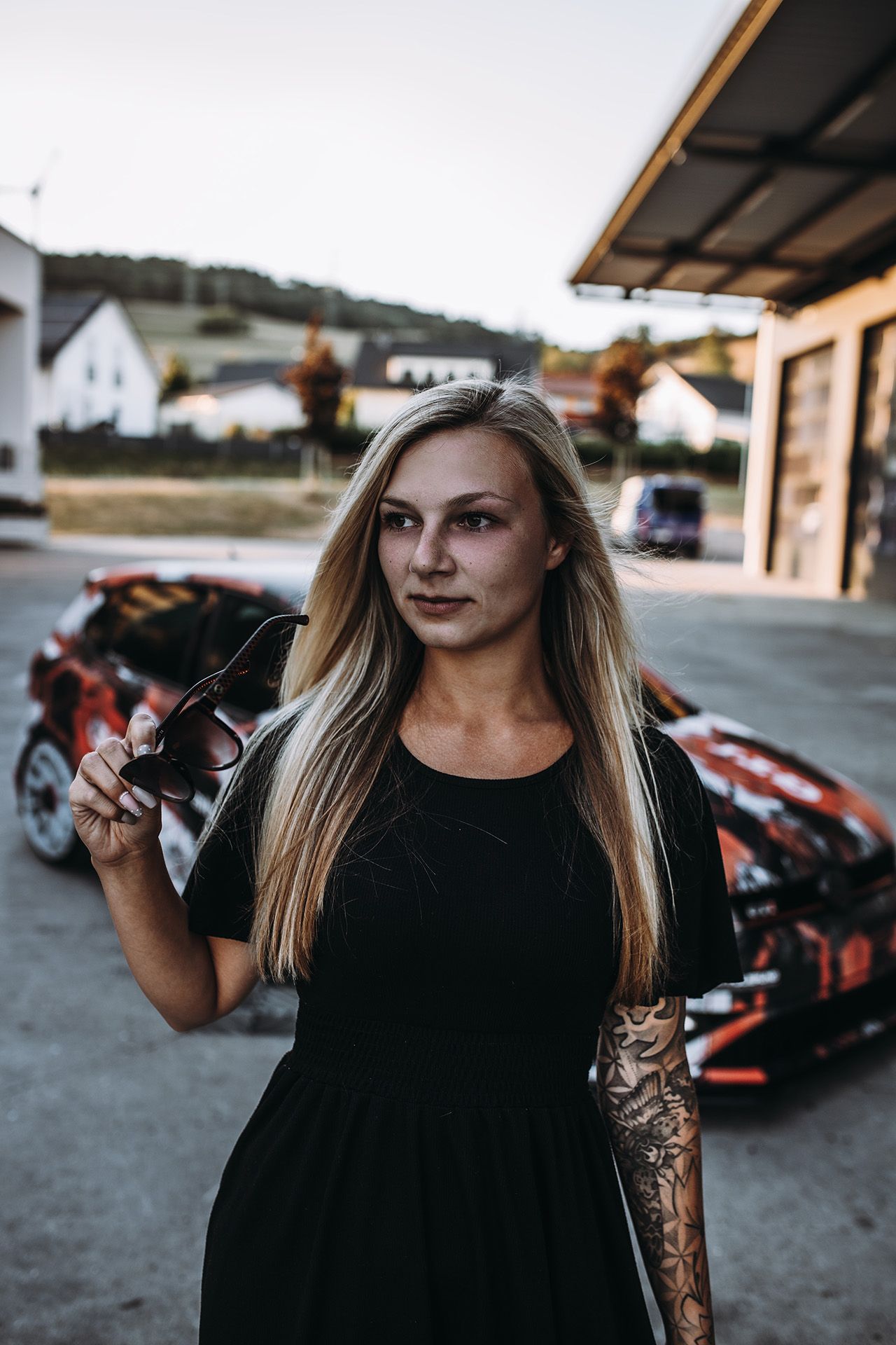 Franziska im schwarzen Kleid mit Sonnenbrille in der Hand, im Hintergrund ihr folierter Polo GTI