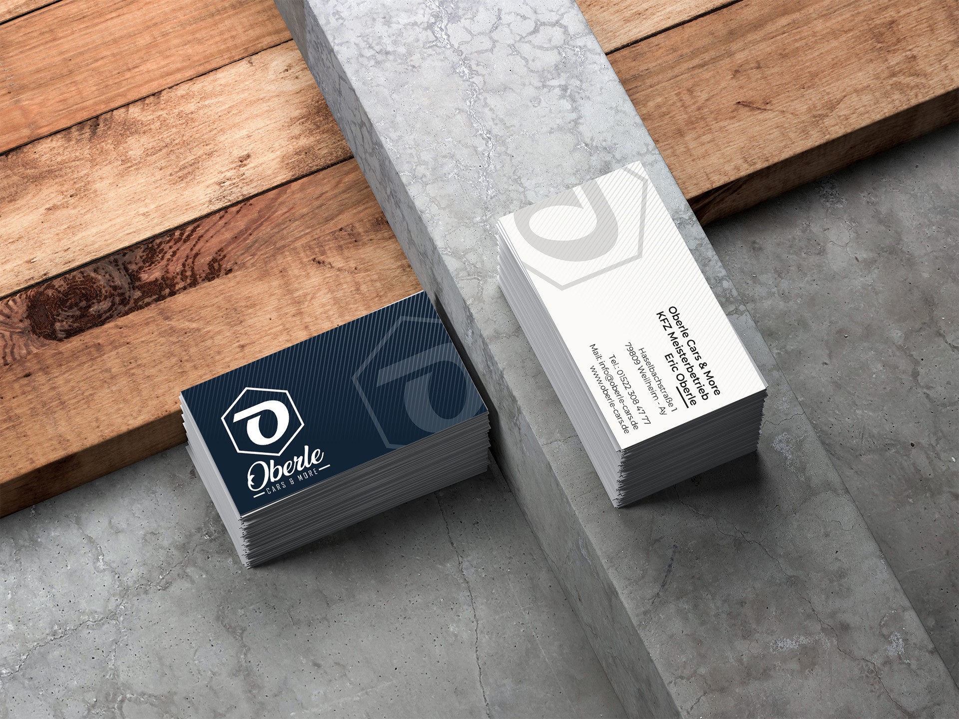 Visitenkarten von Oberle Cars & More mit dem Marken-Logo, auf Holz und Beton inszeniert.