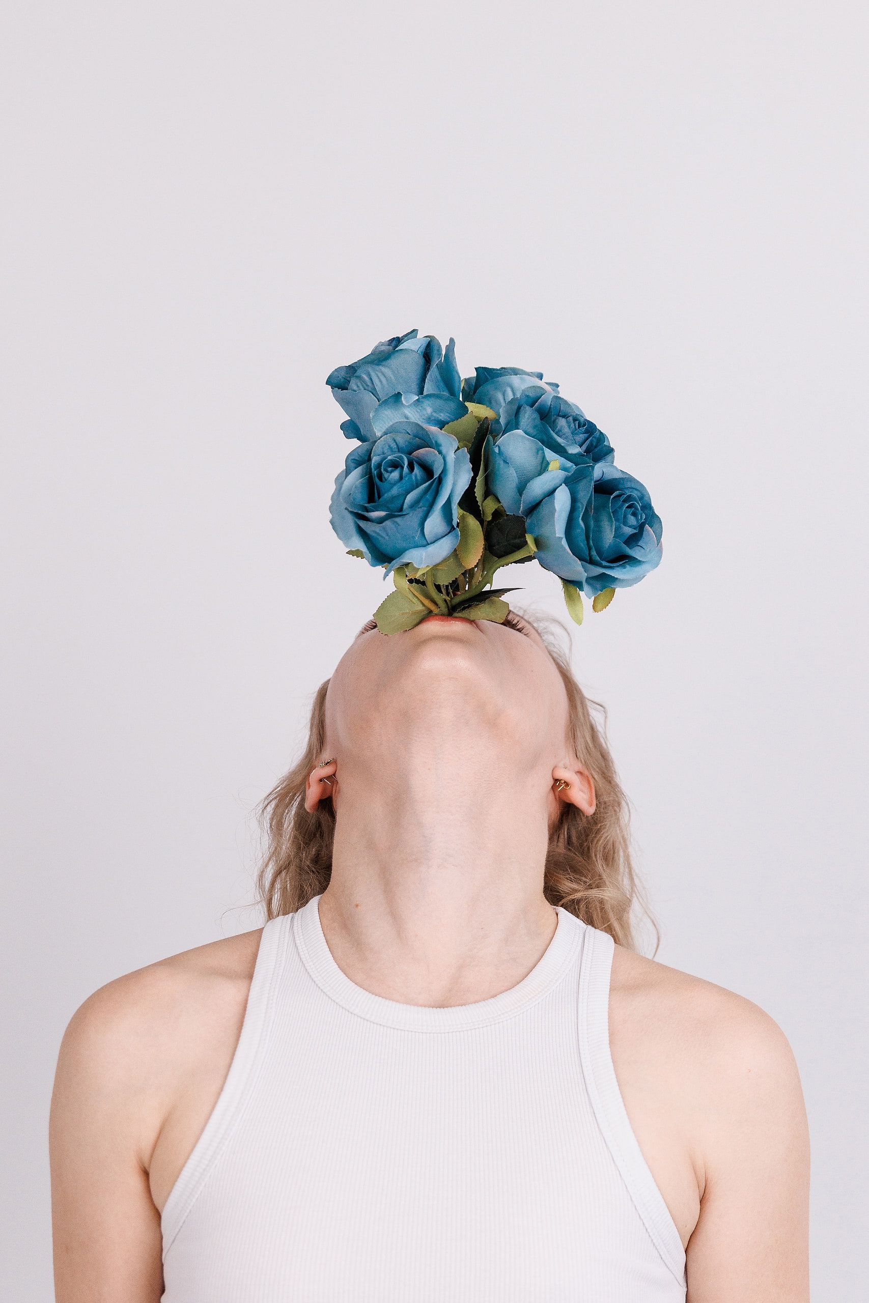 Konzeptportrait: ein Strauß blauer Rosen wächst vor Annettes nach hinten geneigtem Kopf, heller Studiohintergrund.