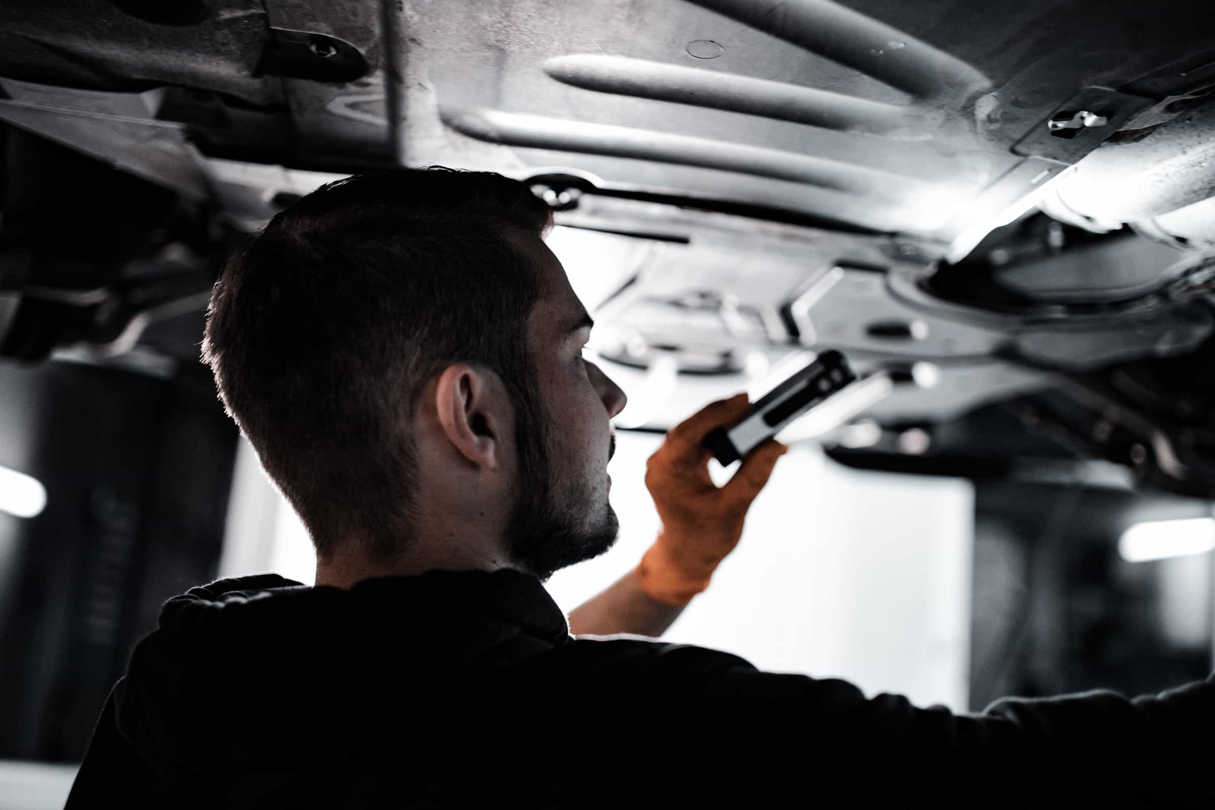 Mechaniker prüft mit einer Lampe den Unterboden eines Fahrzeugs auf der Hebebühne.