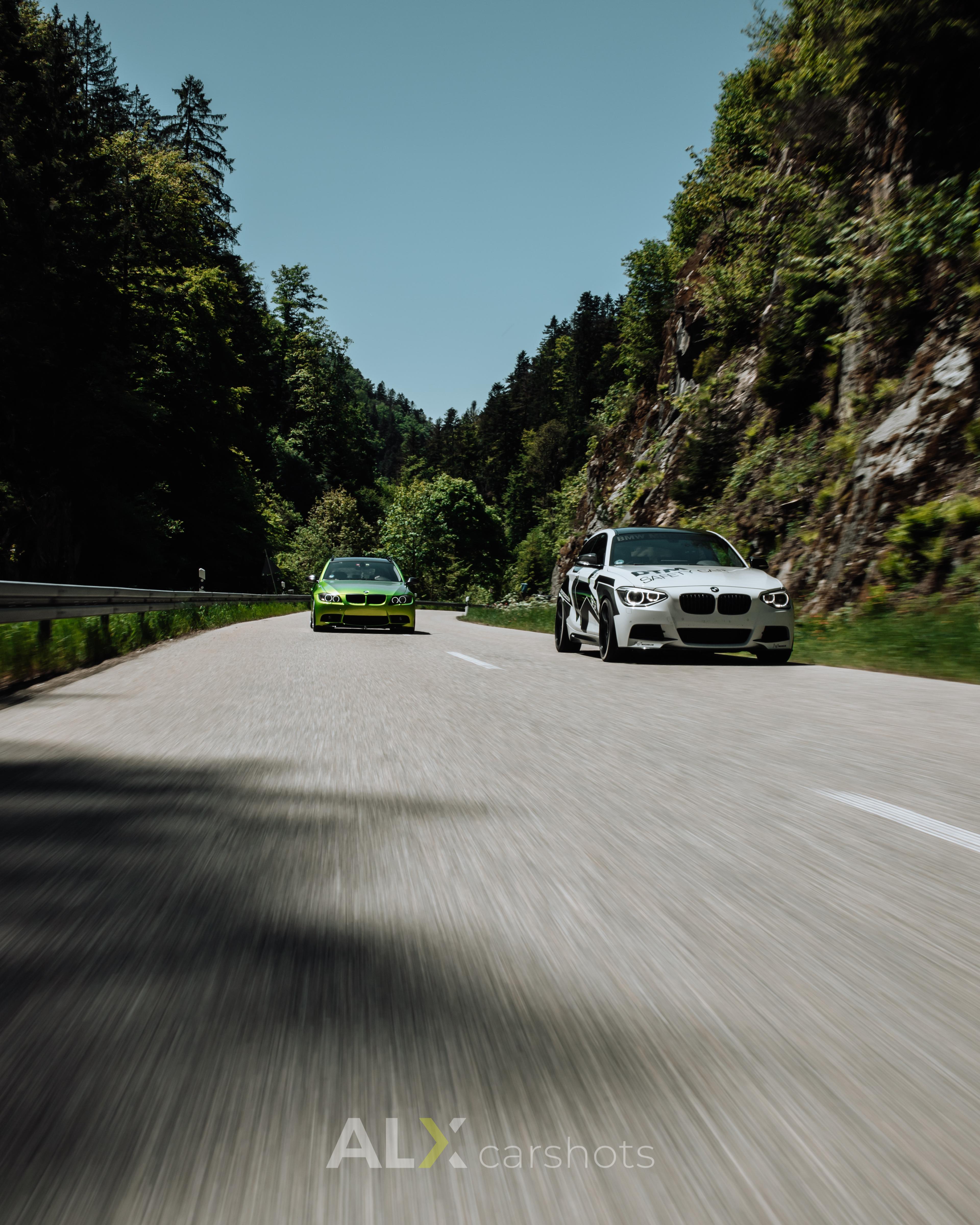 Grüner BMW und weißer BMW 5er nebeneinander als Rollingshot auf einer offenen Schwarzwaldstraße, Asphalt in Bewegung verwischt, Automotive-Aufnahme von aLx-design