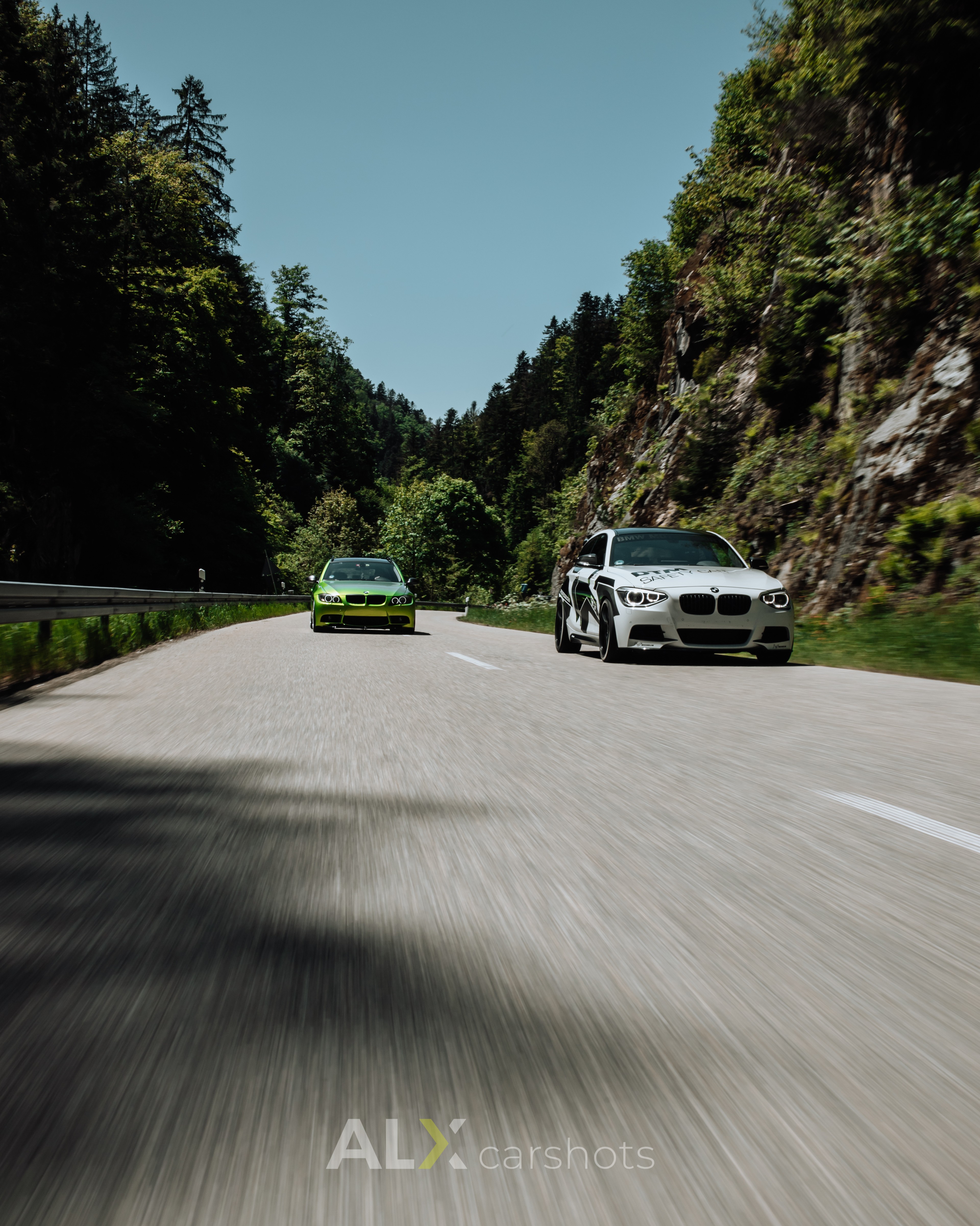 Grüner BMW und weißer BMW 5er nebeneinander als Rollingshot auf einer offenen Schwarzwaldstraße, Asphalt in Bewegung verwischt, Automotive-Aufnahme von aLx-design