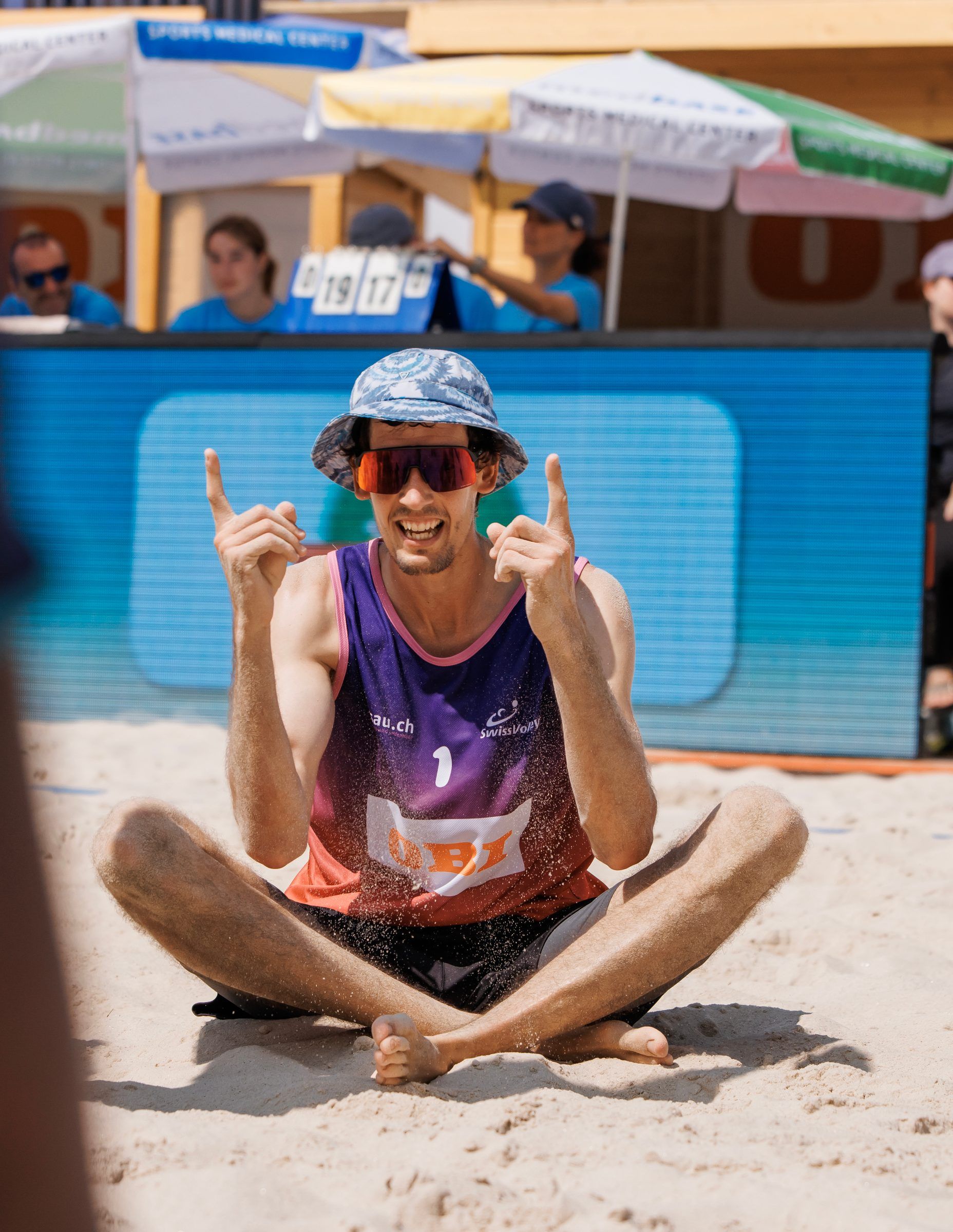 Simon Hagenbuch sitzt im Sand und jubelt mit erhobenen Händen, im Spiel Hagenbuch/Haussener gegen Dillier/Flückiger bei der OBI Beach Tour 2026 in Basel.