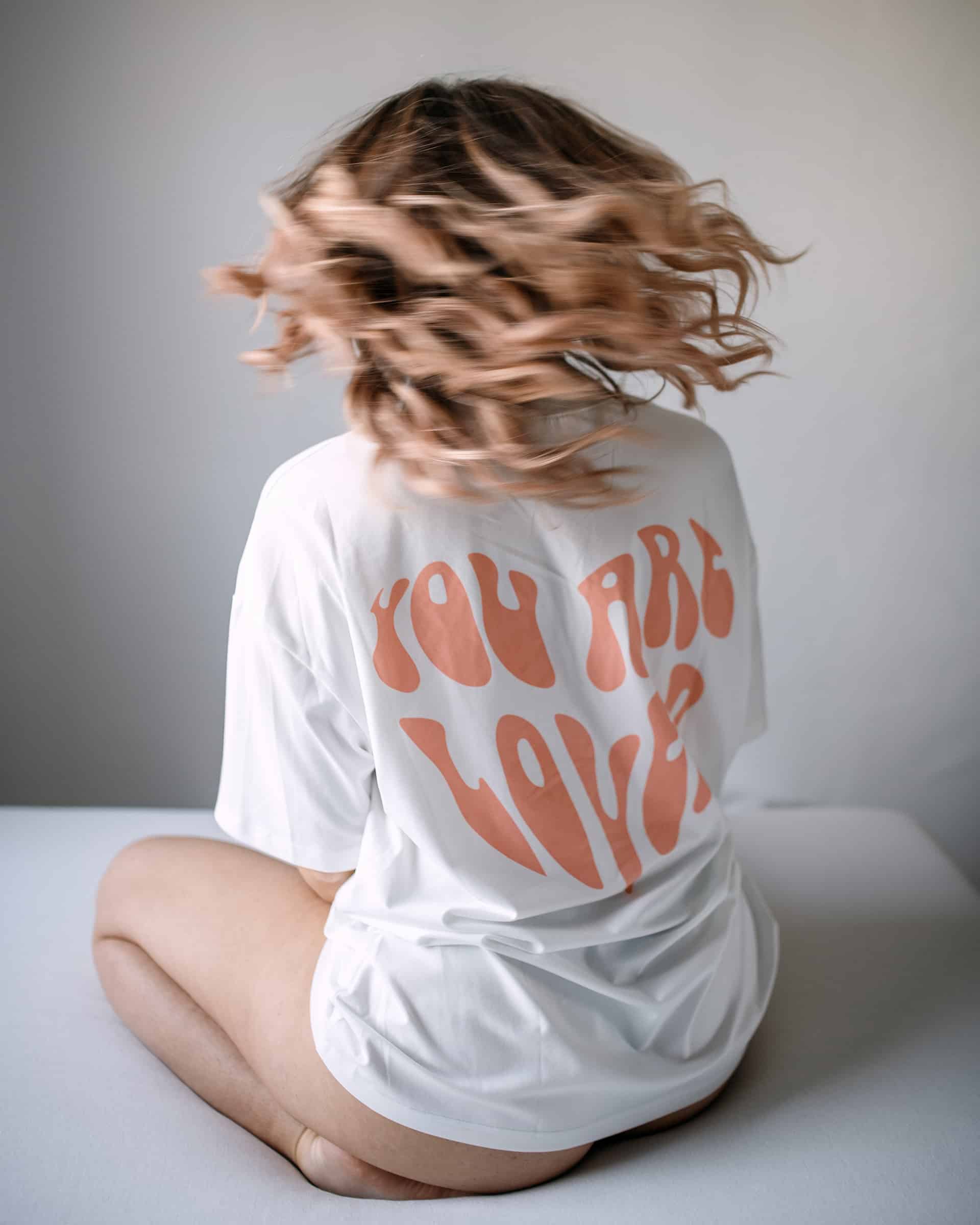 Rückenansicht von Zintle im weißen Shirt mit Aufdruck „You are loved“, Haare in Bewegung