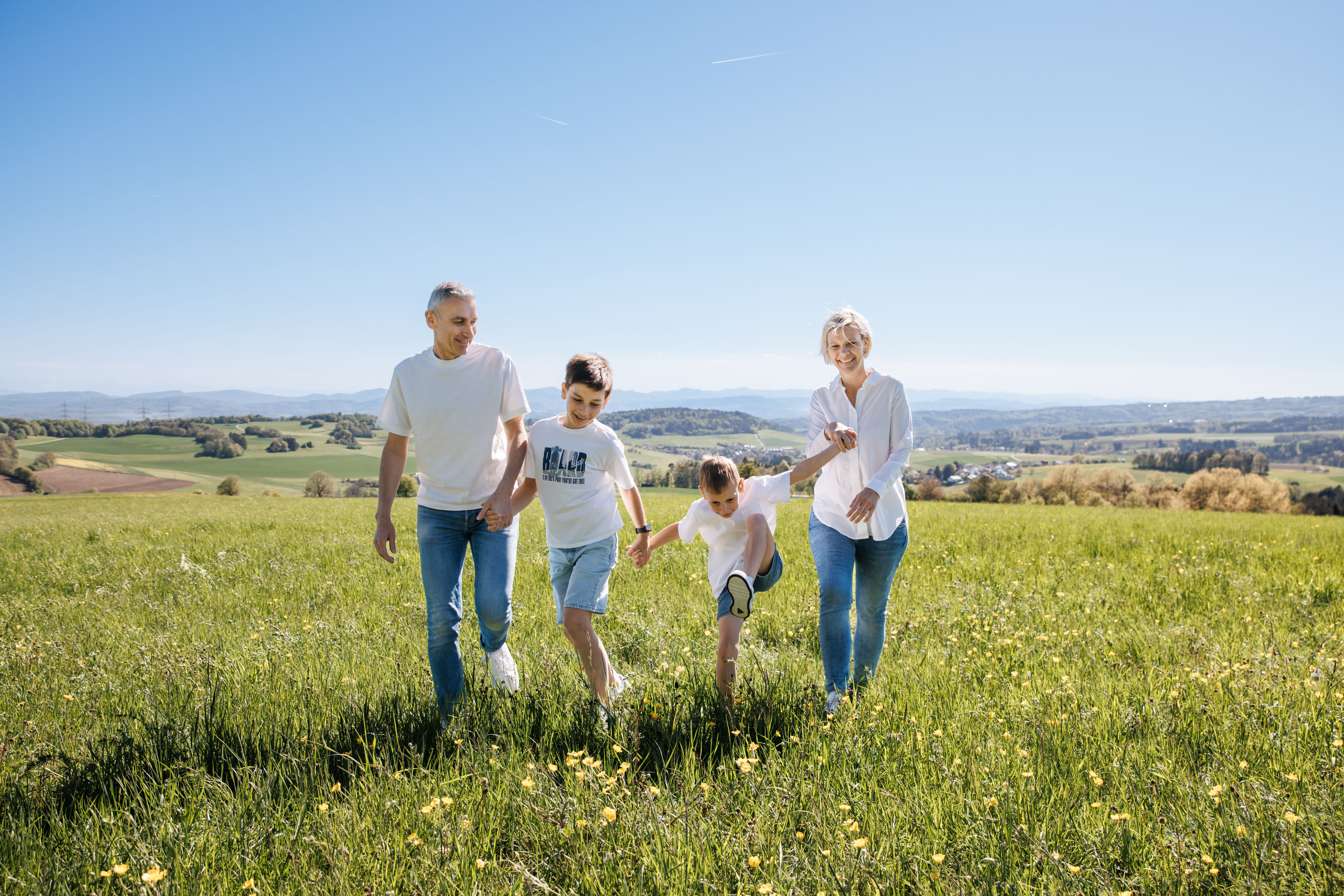 Familie geht gemeinsam durch das hohe Gras einer Wiese in die Ferne