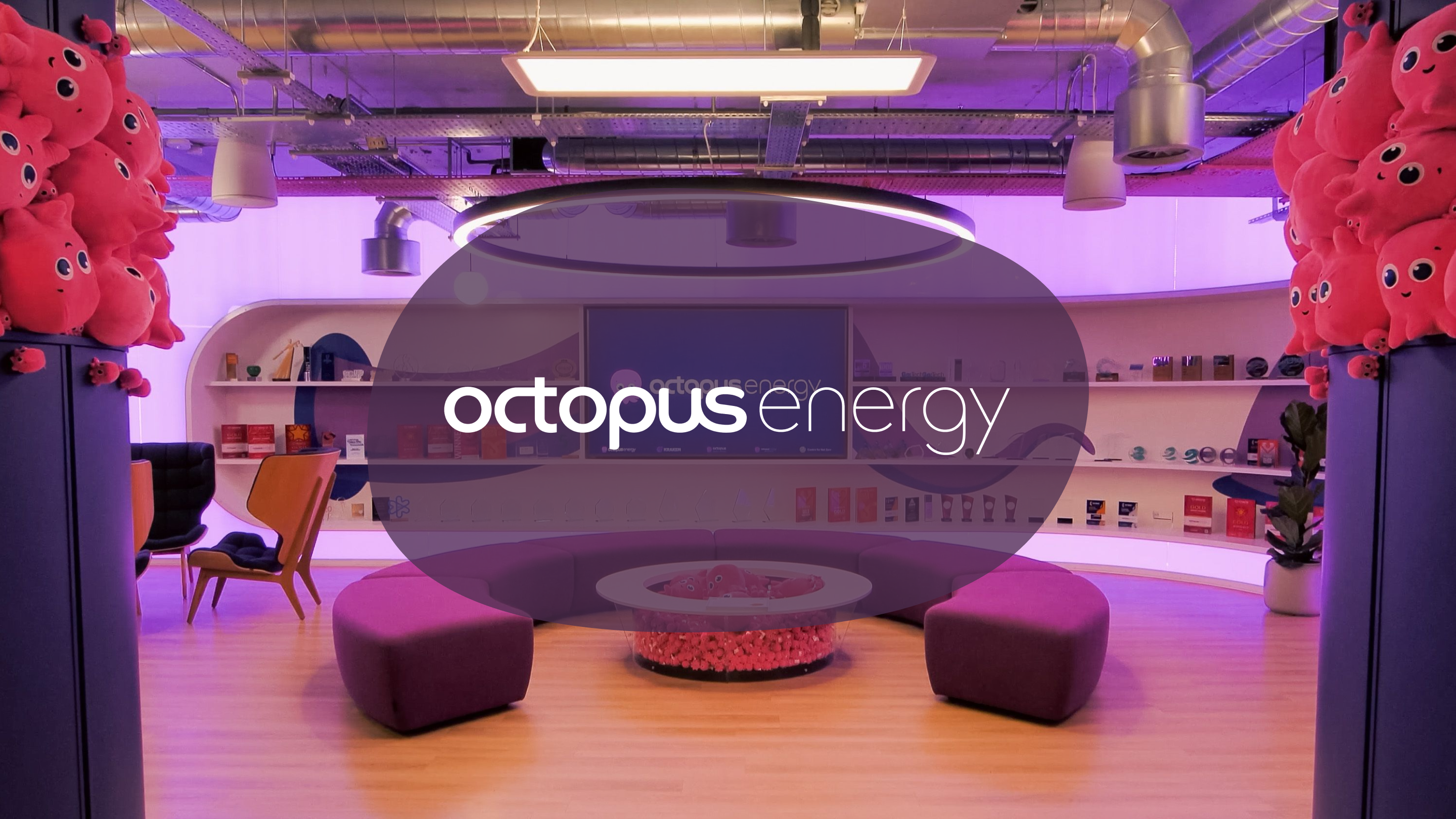 A vibrant, modern lounge area with purple lighting, pink octopus plush toys, curved purple seating, and an "Octopus Energy" logo on a screen.