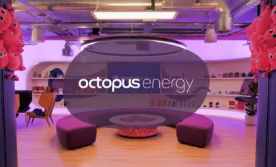 A vibrant, modern lounge area with purple lighting, pink octopus plush toys, curved purple seating, and an "Octopus Energy" logo on a screen.