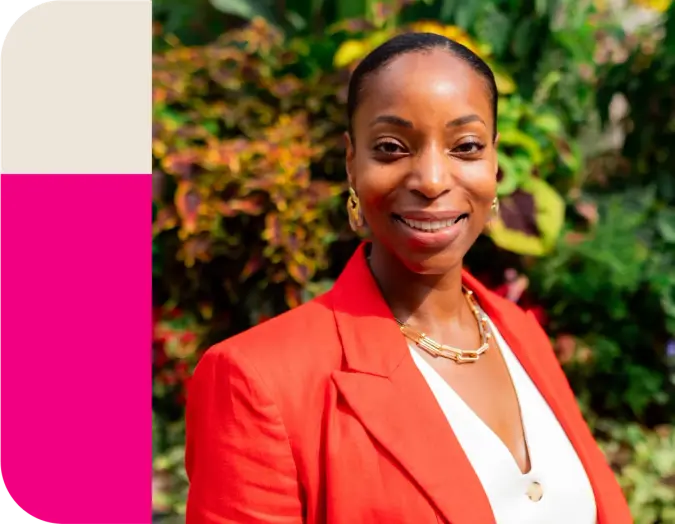 Smiling Black woman in a red blazer against green foliage.
