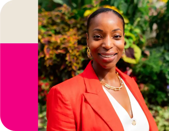 Smiling Black woman in a red blazer against green foliage.