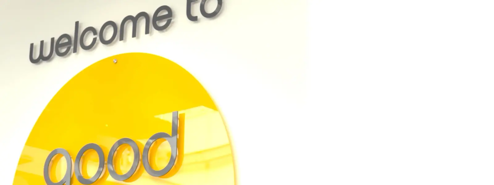 Yellow circular sign with "good energy" in silver letters, mounted below "welcome to" on a white wall.