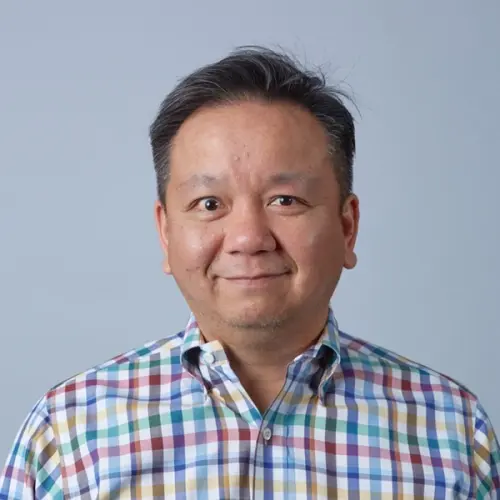Headshot of a smiling man in a colorful plaid shirt.