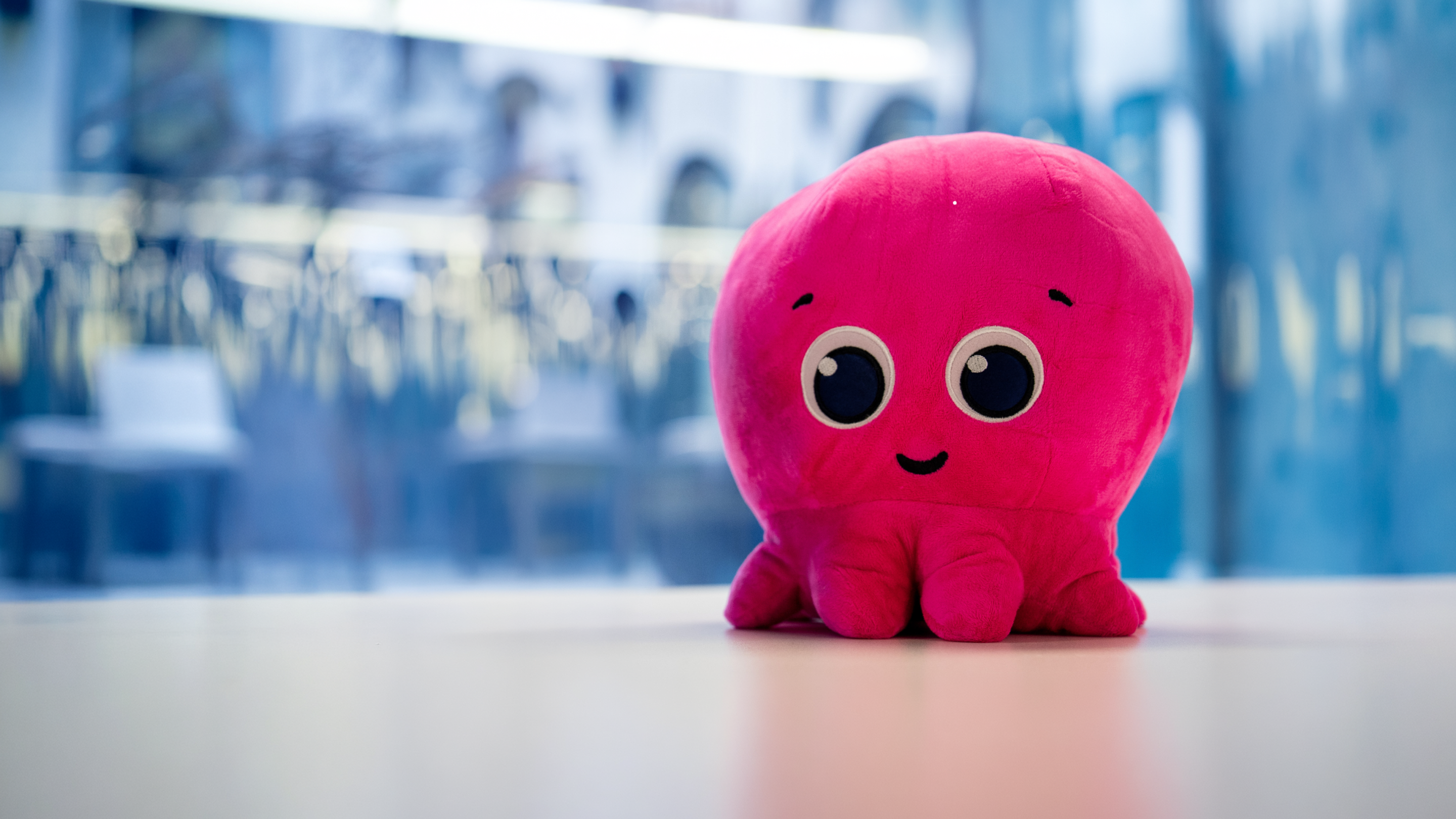 A pink octopus plush toy with big eyes and a smile sits on a table.