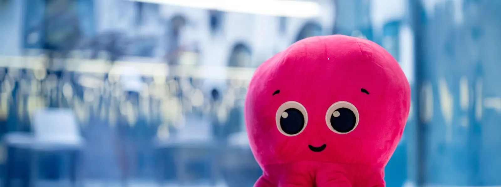 A pink octopus plush toy with big eyes and a smile sits on a table.