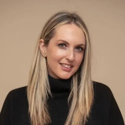 A smiling woman with long blonde hair wearing a black turtleneck.