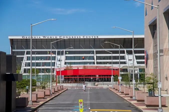 Exterior of the Georgia World Congress Center building with a prominent red pedestrian bridge and a paved entrance road under a blue sky.