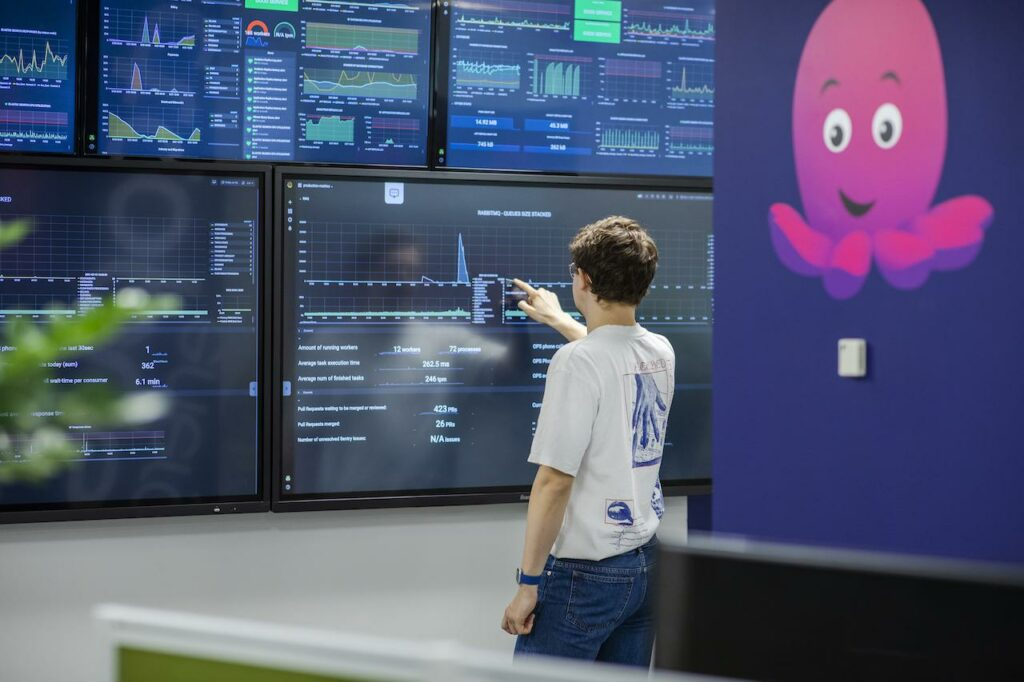 A young man points at large data dashboards on a wall