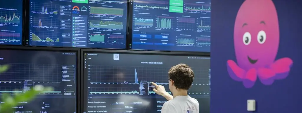 A young man points at large data dashboards on a wall
