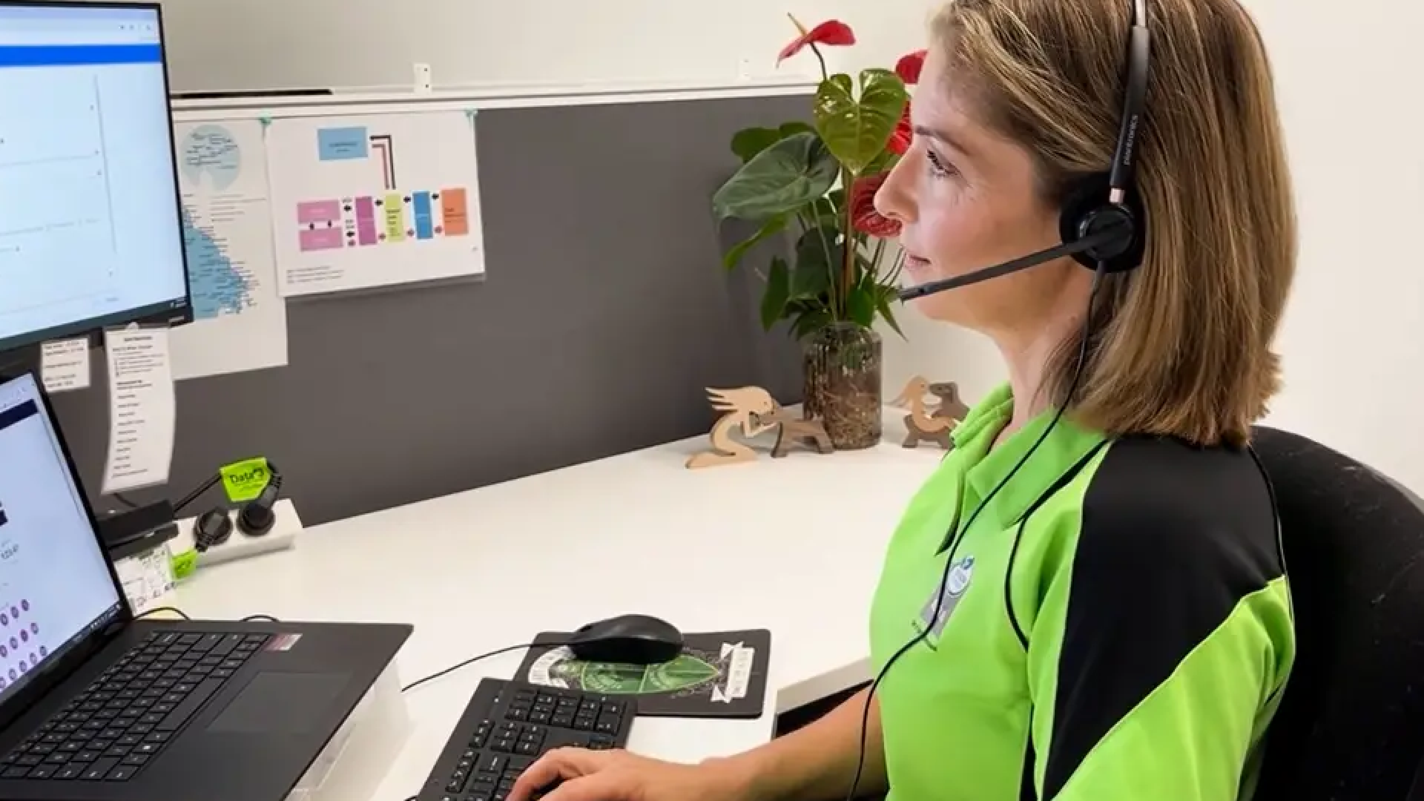 A woman wearing a headset works at a computer desk.
