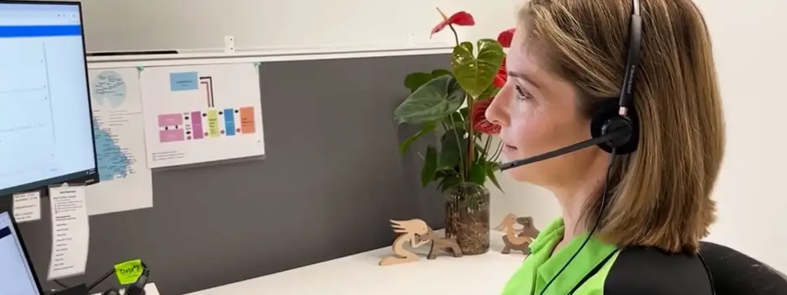 A woman wearing a headset works at a computer desk.
