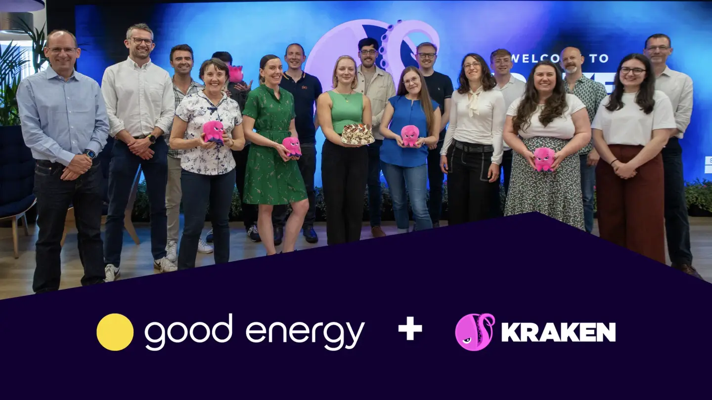 A group of smiling people, some holding pink kraken plush toys, stand in front of a screen with a kraken image and "WELCOME TO". Good Energy and Kraken logos are at the bottom.