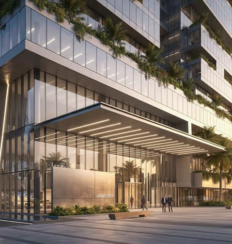 Modern glass high-rise building with green terraces, palm trees, and a brightly lit entrance.