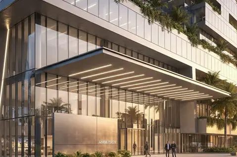Modern glass high-rise building with green terraces, palm trees, and a brightly lit entrance.