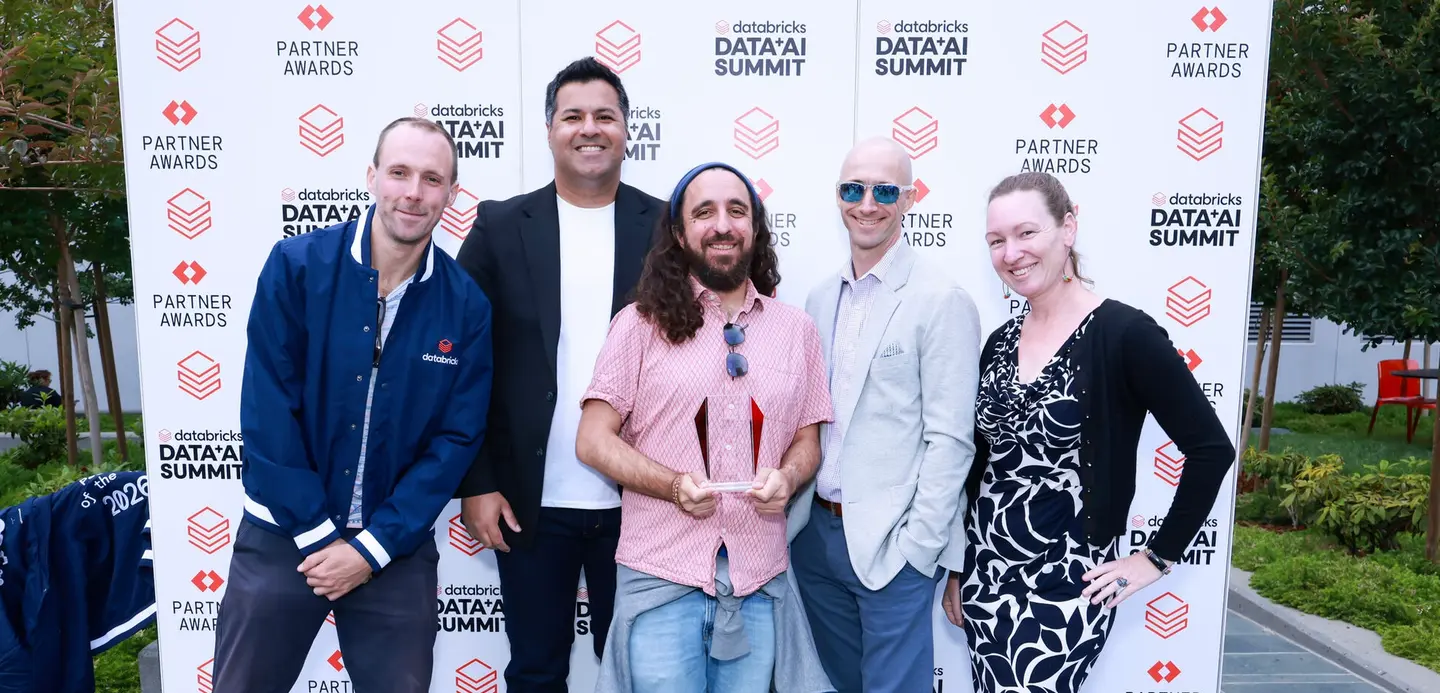 Kraken and Databricks employees stand in front of a Databricks Partner Awards banner, one holding a trophy.