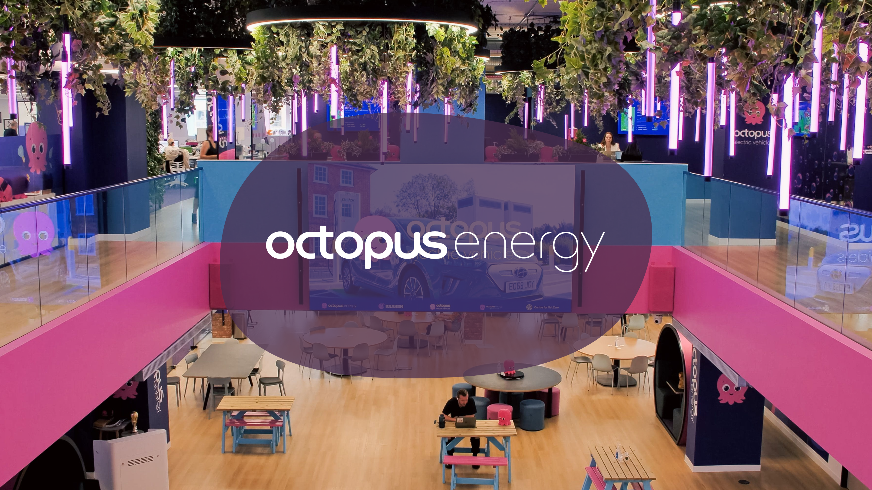 Vibrant, multi-level Octopus Energy office with pink and blue decor, hanging plants, purple lights, and people working. The Octopus Energy logo is prominent.
