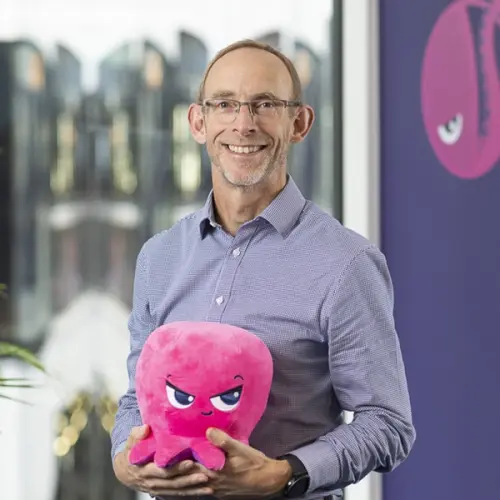 A smiling man holding a pink angry octopus plushie.