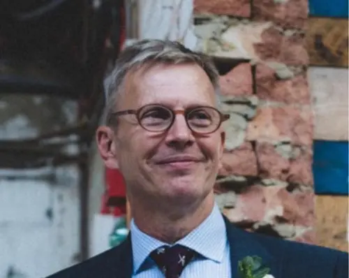Smiling man with gray hair and glasses, wearing a suit and tie.