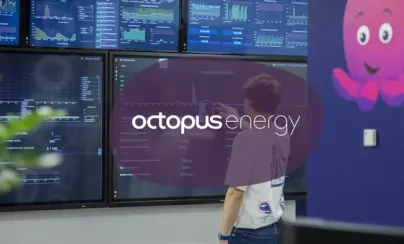 A person interacting with a wall of data screens, branded with Octopus Energy and featuring their octopus mascot.