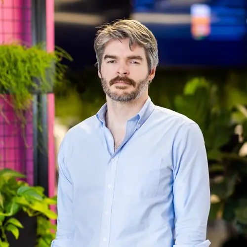 A man with graying hair and a beard wears a light blue shirt.