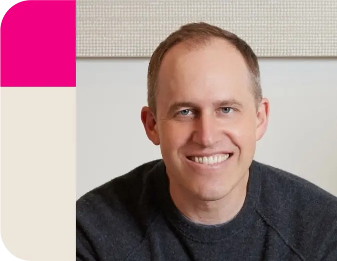 A smiling man in a dark sweater beside a pink and beige vertical graphic.