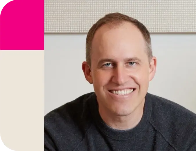 A smiling man in a dark sweater beside a pink and beige vertical graphic.