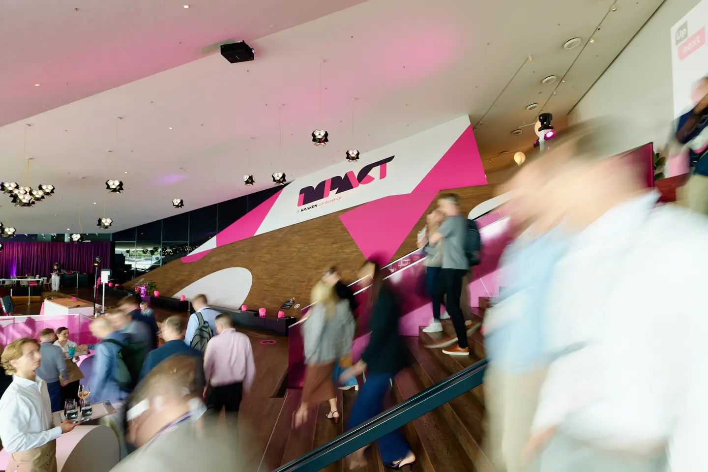 Attendees with motion blur moving through a modern event venue with pink and white "IMPACT" branding.