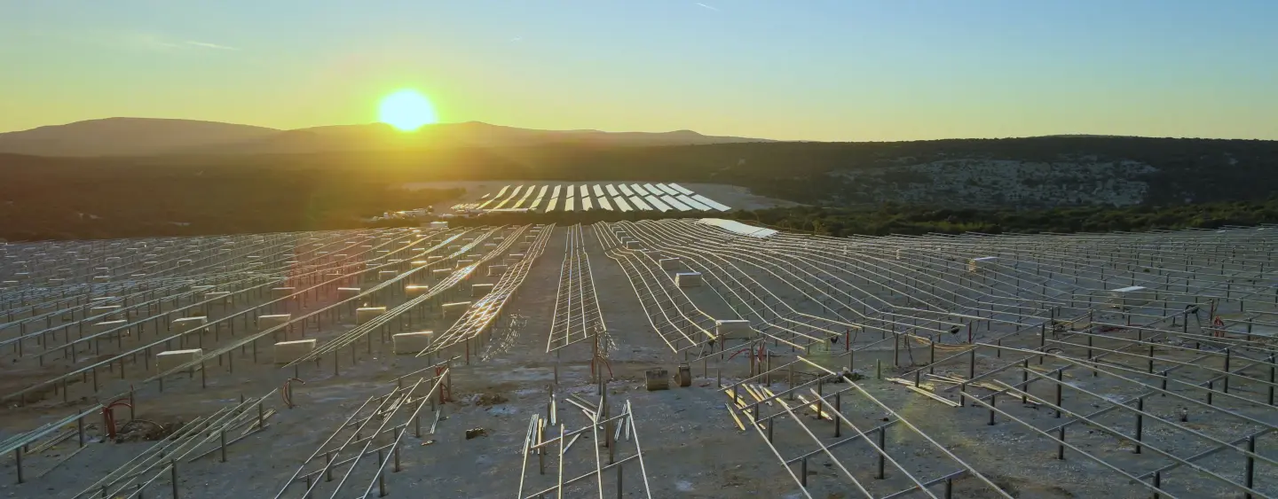 Rows of solar panel mounting frames under construction at sunset, with installed panels visible in the distance.