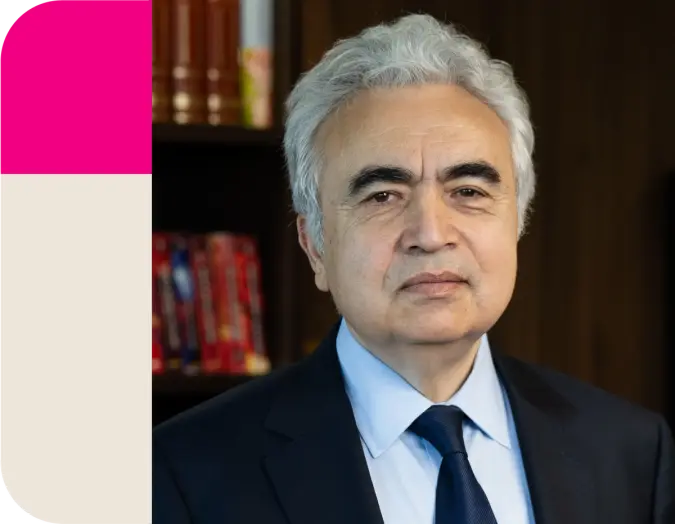 A man with gray hair and a dark suit looks forward, with a magenta and cream block on the left.