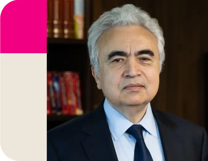 A man with gray hair and a dark suit looks forward, with a magenta and cream block on the left.