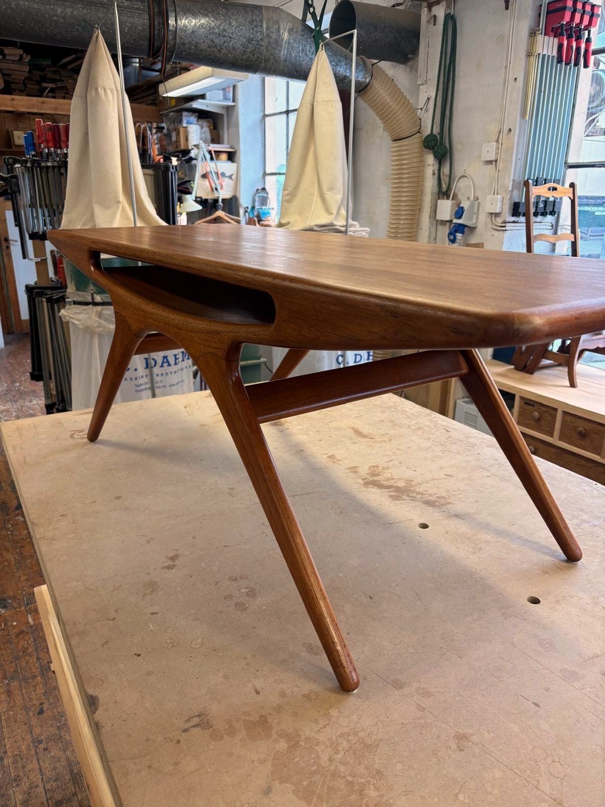 Sofabordet i teak sett skrått fra siden, med de skrå bena og hylla under platen.