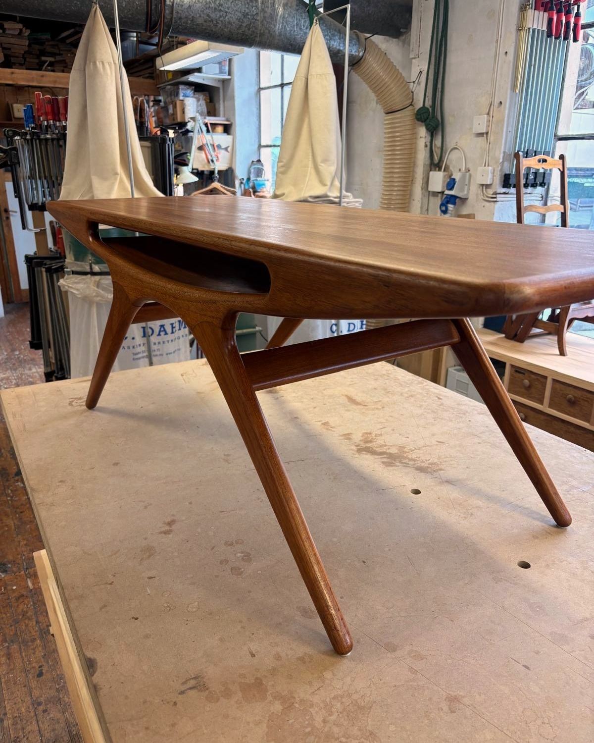 Sofabordet i teak sett skrått fra siden, med de skrå bena og hylla under platen.