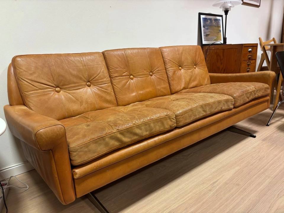 Hele sofaen sett forfra, tre seter i cognacfarget skinn.