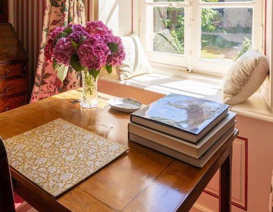 Chambre aux Fleurs: hydrangeas and art books on a table by a sunny window seat overlooking the garden