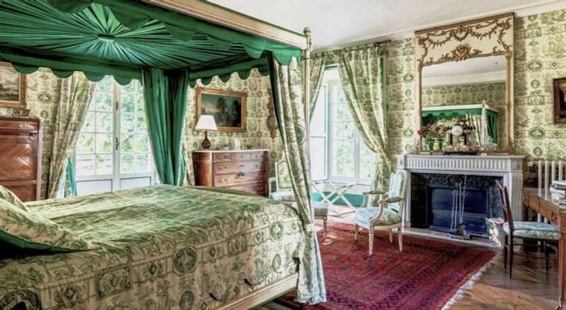 Suite bedroom with green canopy bed, matching fabric walls, red rug and marble fireplace