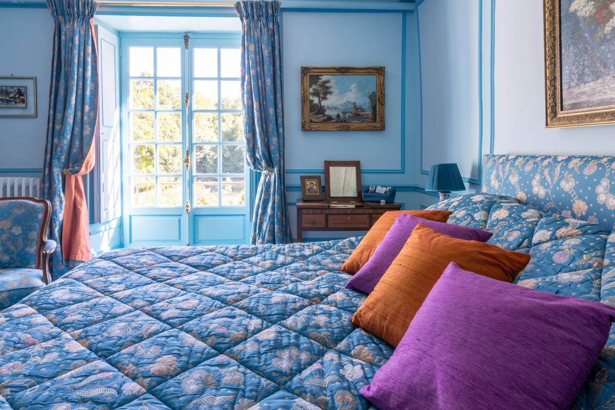 Chambre Turquoise: quilted blue floral bed with purple and orange cushions, French window