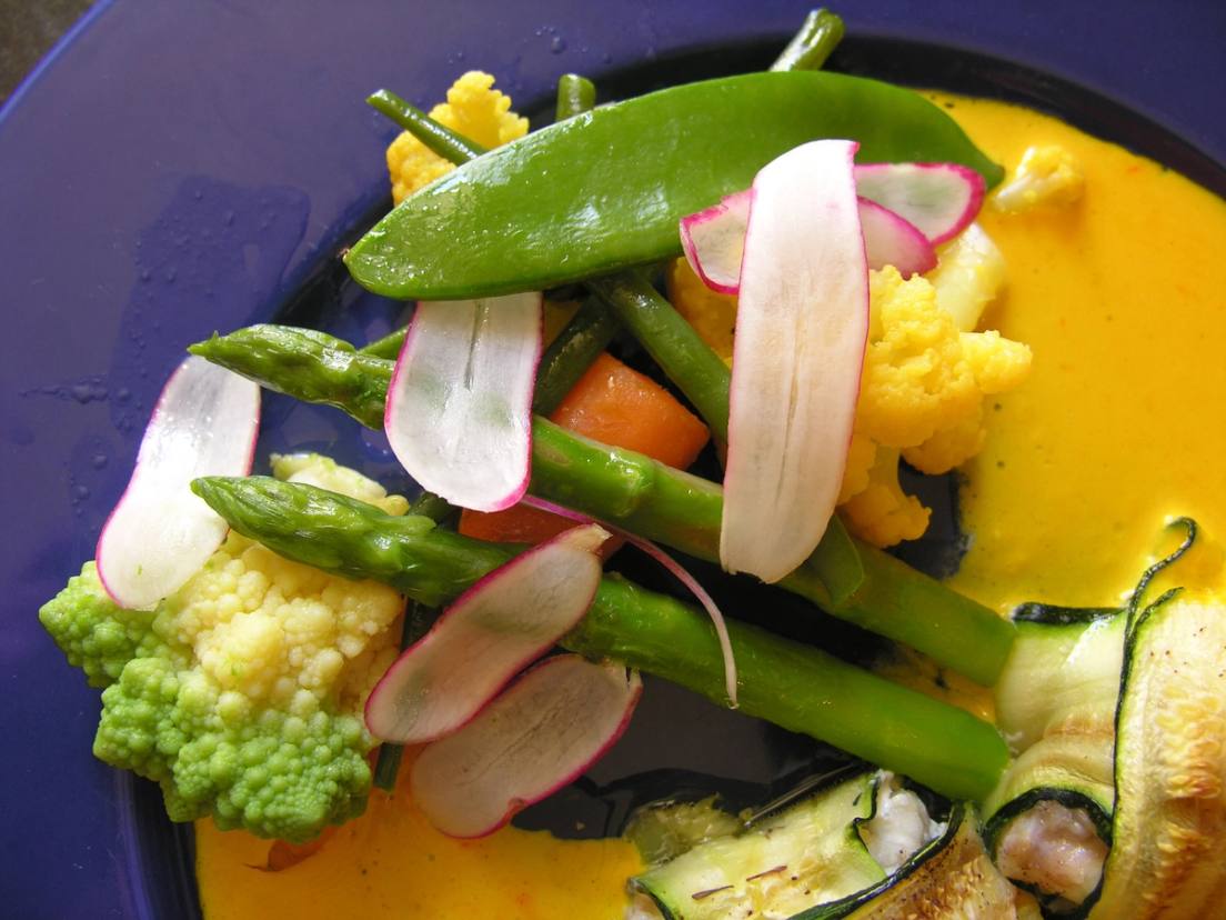 Assiette de légumes printaniers : asperges, romanesco, courgette et radis sur une sauce dorée