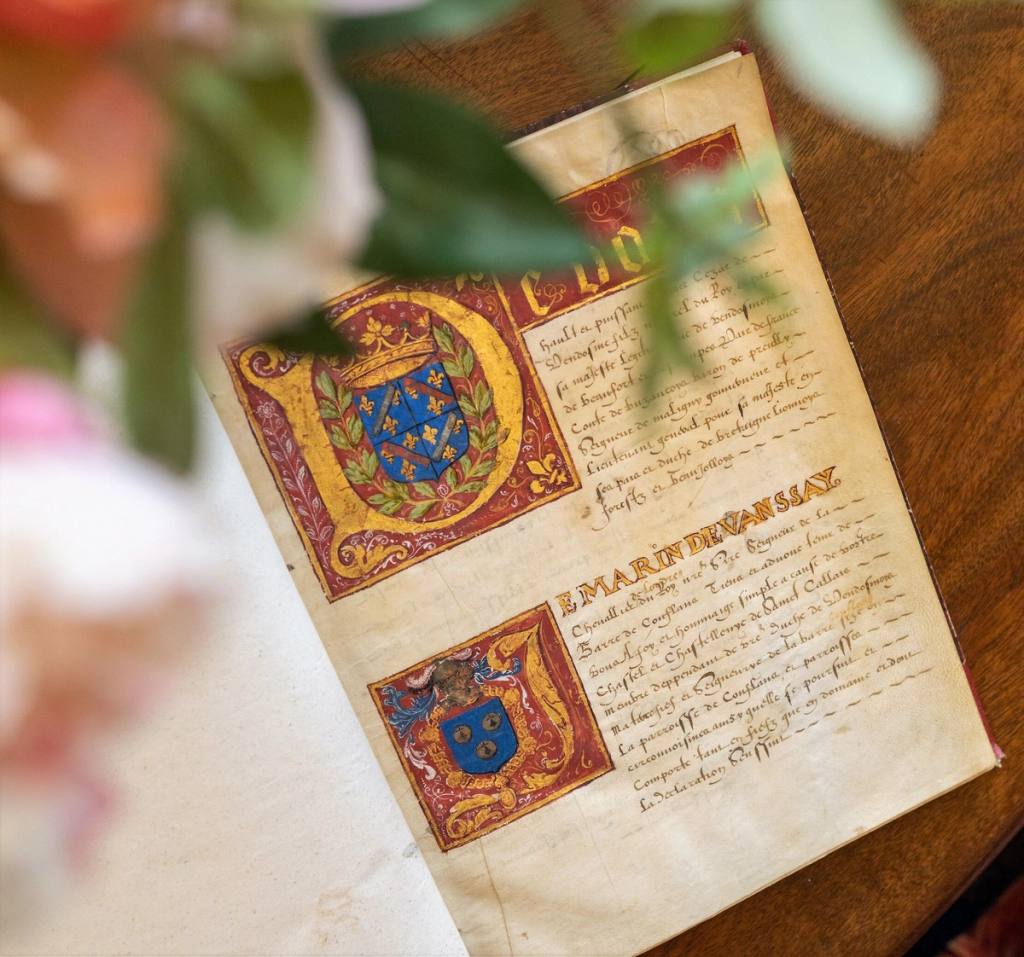 Illuminated manuscript from 1603 open on a table, with painted coats of arms and gilded initials