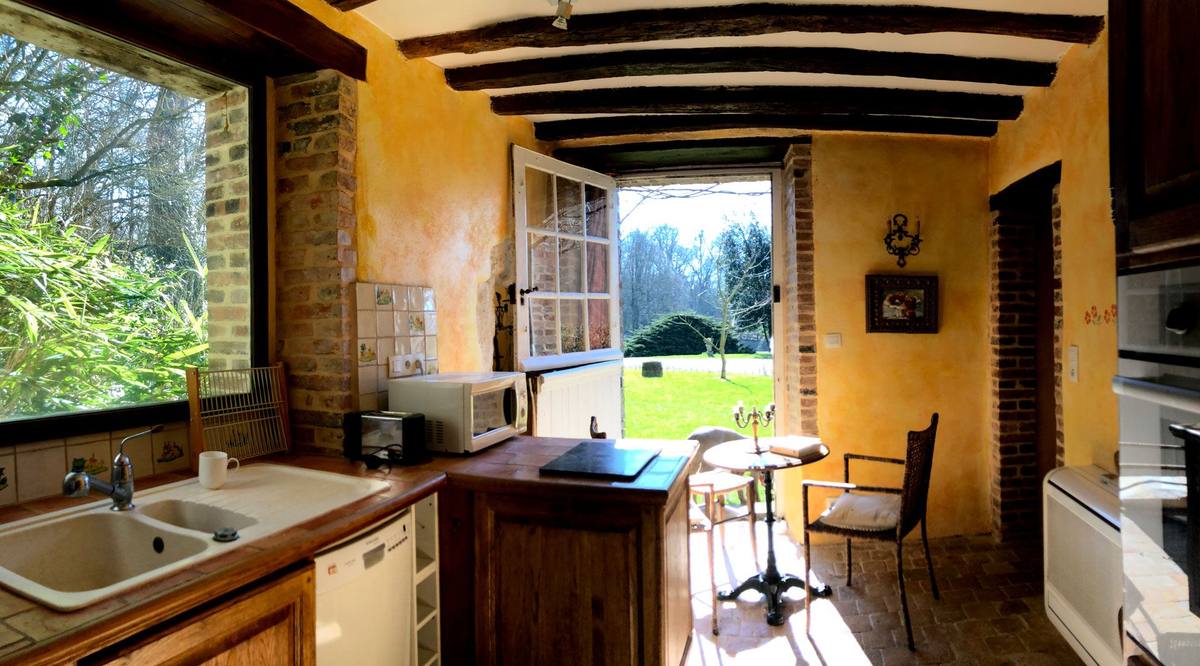 Cottage Les Glycines kitchen with beamed ceiling, sink by the window and door open onto the lawn